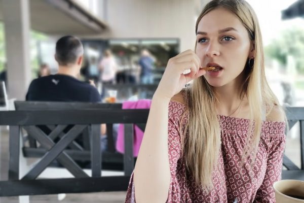 Blonde woman in a patterned top enjoying a snack at an outdoor café in Lithuania.