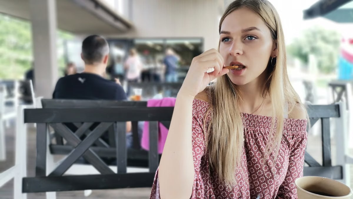 Blonde woman in a patterned top enjoying a snack at an outdoor café in Lithuania.